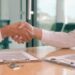 A close-up of two professionals shaking hands over signed documents on a desk, symbolizing a successful deal and the ability to sell with confidence.