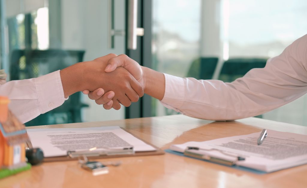 A close-up of two professionals shaking hands over signed documents on a desk, symbolizing a successful deal and the ability to sell with confidence.