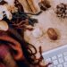 Flat lay of a laptop keyboard beside dried flowers, pinecones, and a textured scarf arranged on a warm-toned surface.