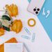 A flat lay on a blue and white background featuring yellow roses, a smartphone, wireless earbuds, blue paperclips, and a notepad titled "Top Three Priorities" with a pen.