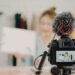 A professional camera with a furry microphone filming a woman holding a white sign, illustrating social media content creation.