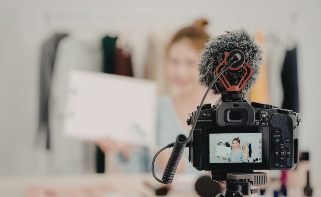 A professional camera with a furry microphone filming a woman holding a white sign, illustrating social media content creation.