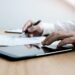 Close-up of a business professional's hands using a digital tablet and reviewing financial growth charts with a pen on a wooden office desk.