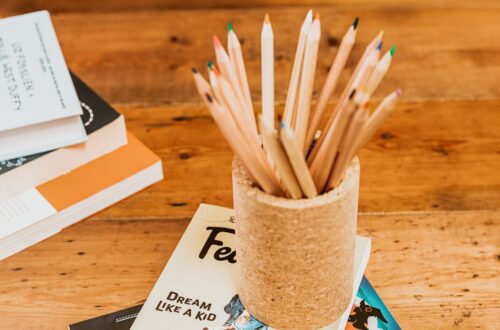 A cylindrical cork pencil holder filled with colored pencils sitting on a book titled "Dream Like a Kid" on a wooden table.